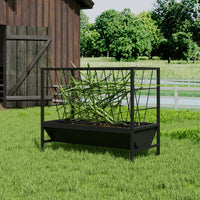 Black metal planter with green plants in front of a wooden shed and greenery