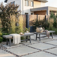 Outdoor patio with two wooden benches, plants, and a lantern on a stone patio.