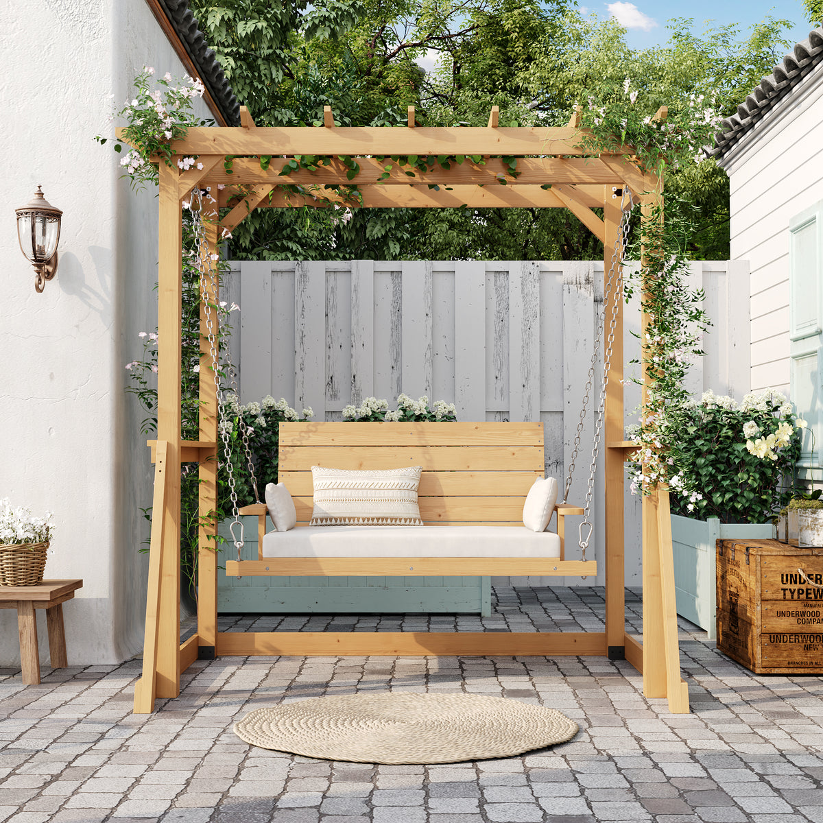 Wooden pergola with a bench on a patio area with plants and a white wall in the background