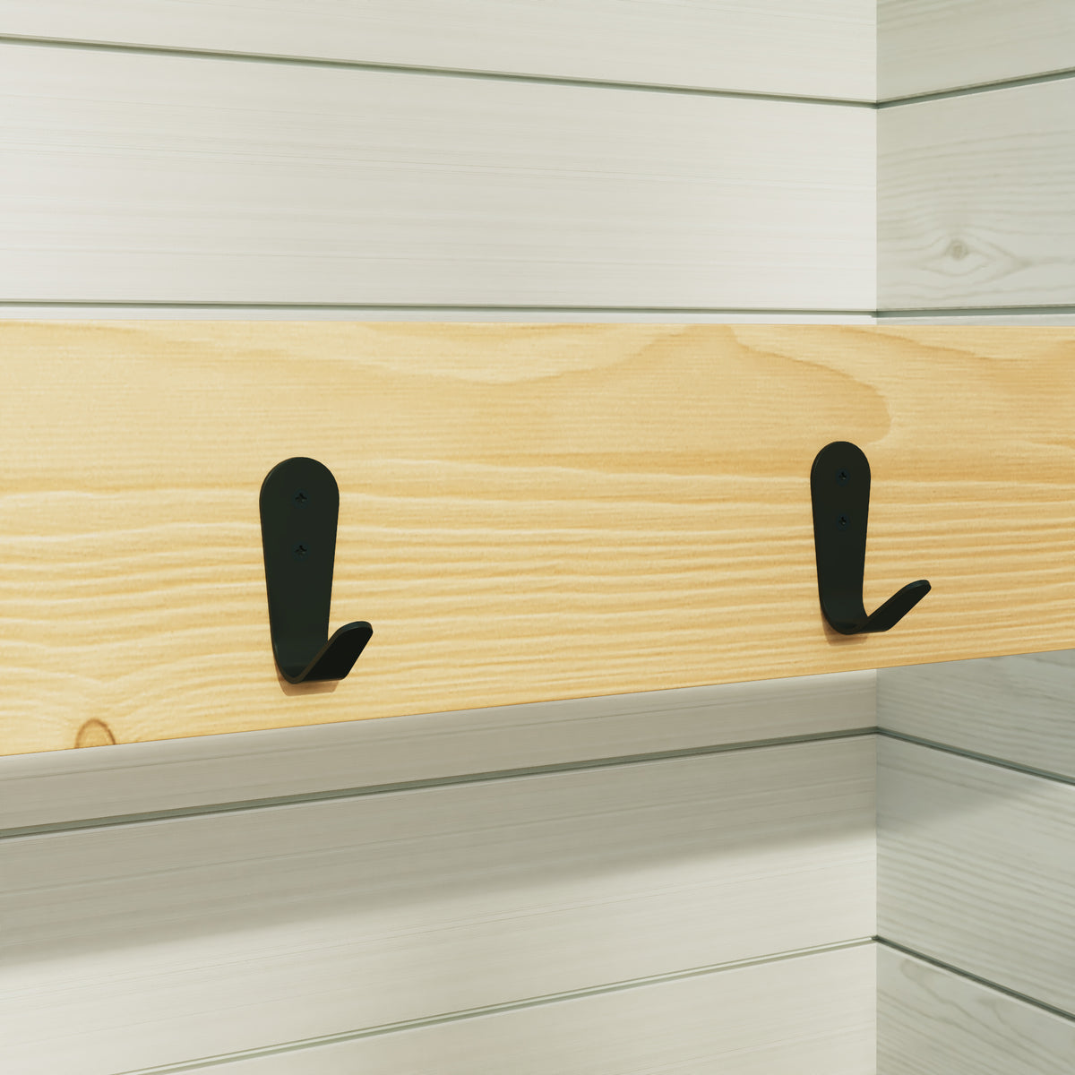 Two black hooks on a wooden shelf against a white wall