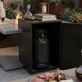 Outdoor setting with a propane tank inside a cabinet next to a fire pit and food platter.