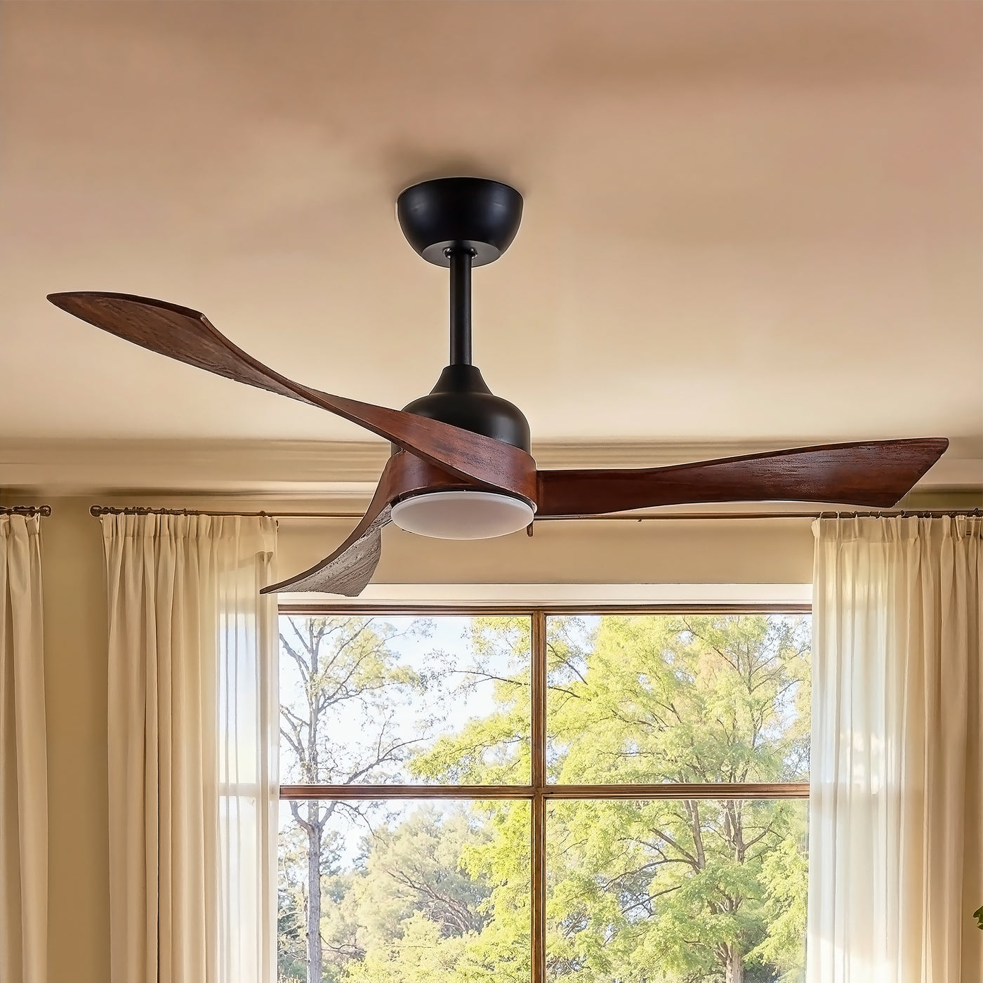 Ceiling fan with wooden blades in a room with a window showing trees outside