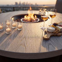 Outdoor setting with a fire pit, candles, wine glasses, and cheese platter on a wooden table.