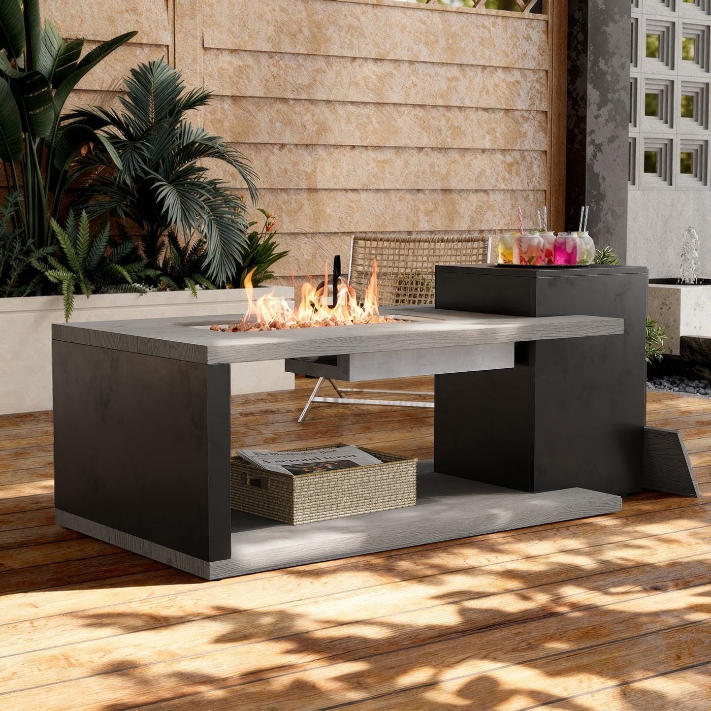 Modern outdoor fire pit table with flames on a wooden deck, surrounded by plants and a building.