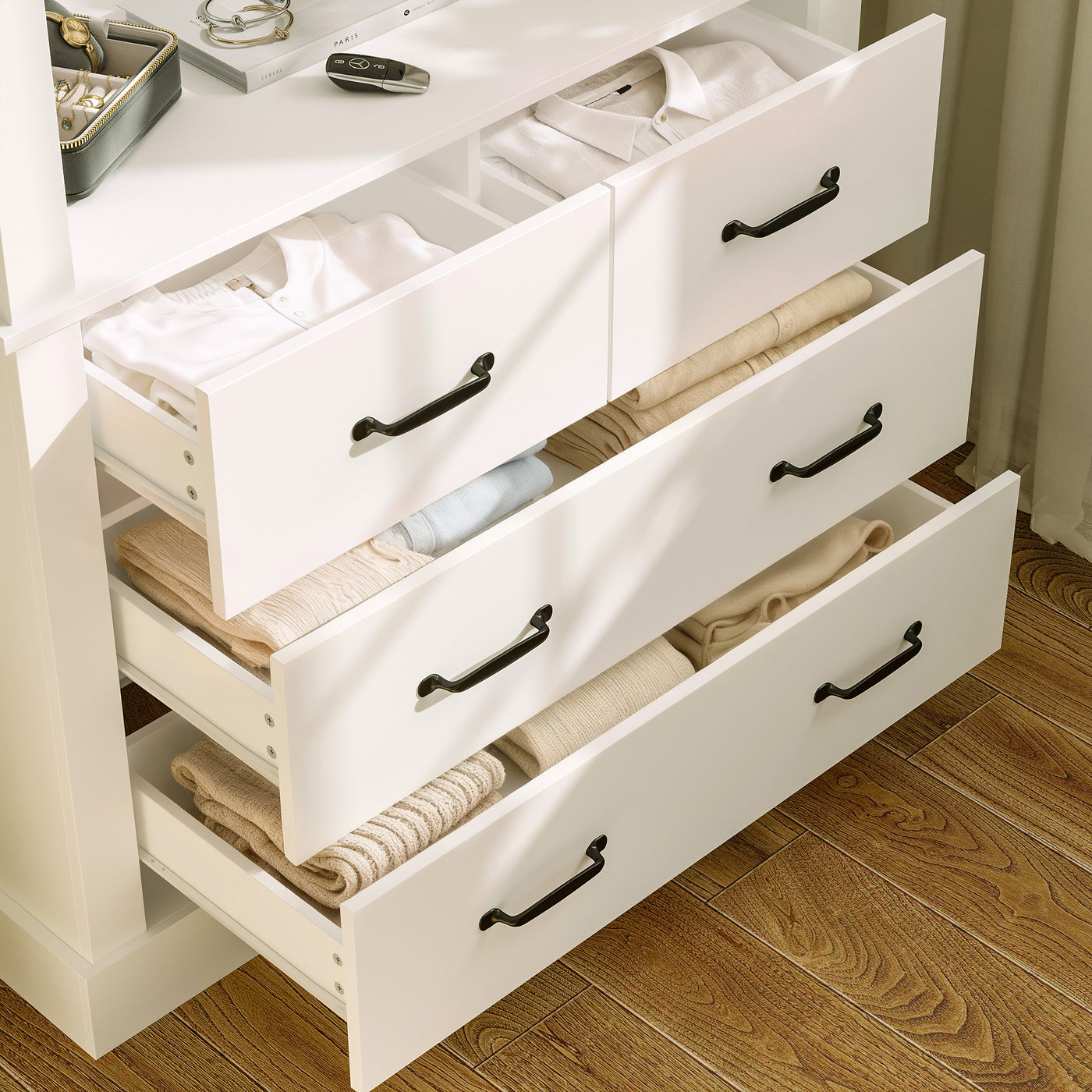 White dresser with open drawers containing folded clothes on a wooden floor.