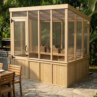 Wooden greenhouse with glass panels on a stone patio, surrounded by outdoor furniture and plants.