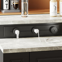 Black power strip with multiple outlets on a kitchen counter with appliances and bottles in the background.