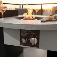 Outdoor fire pit table with flames, wine glasses, and cheese board on a patio.