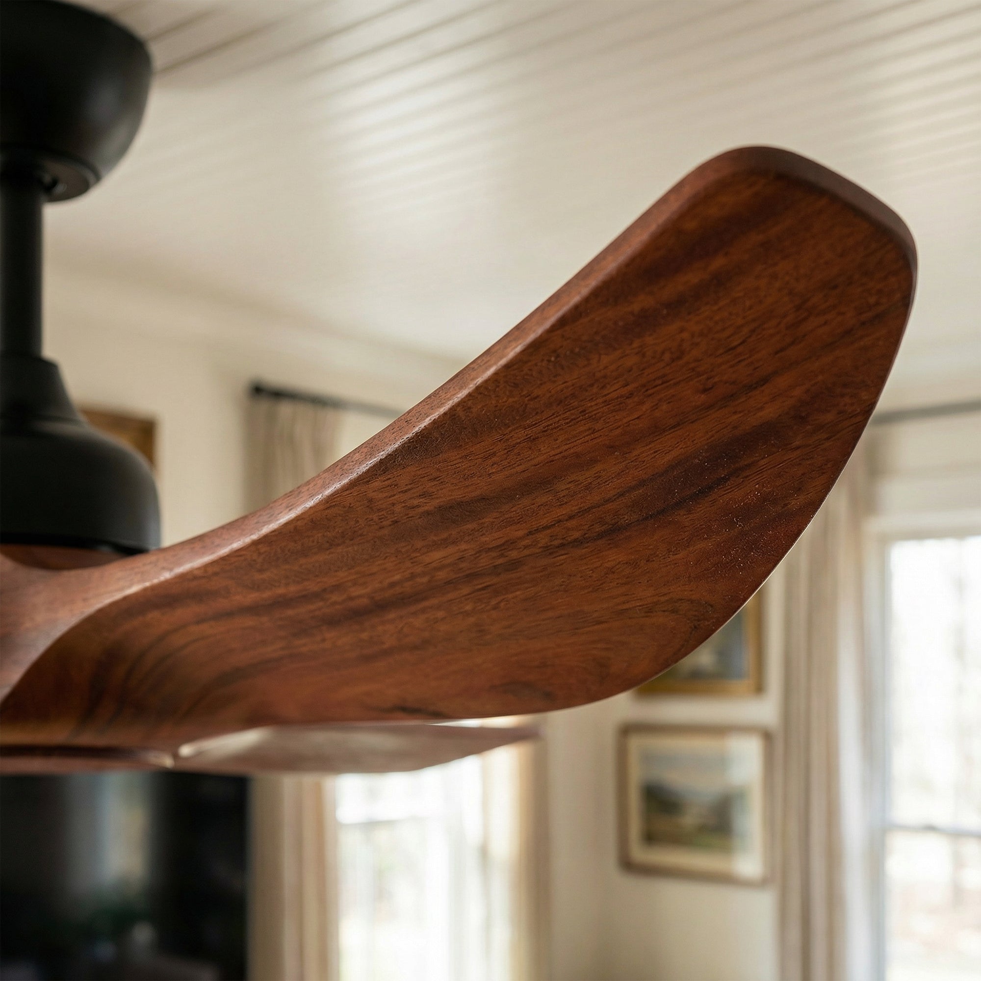 Close-up of a wooden ceiling fan blade with a blurred room background