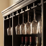 Wine glasses hanging from a rack above wine bottles in a cabinet.