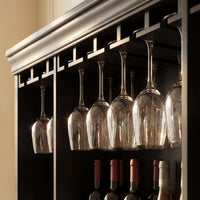Wine glasses hanging from a rack above wine bottles in a cabinet.