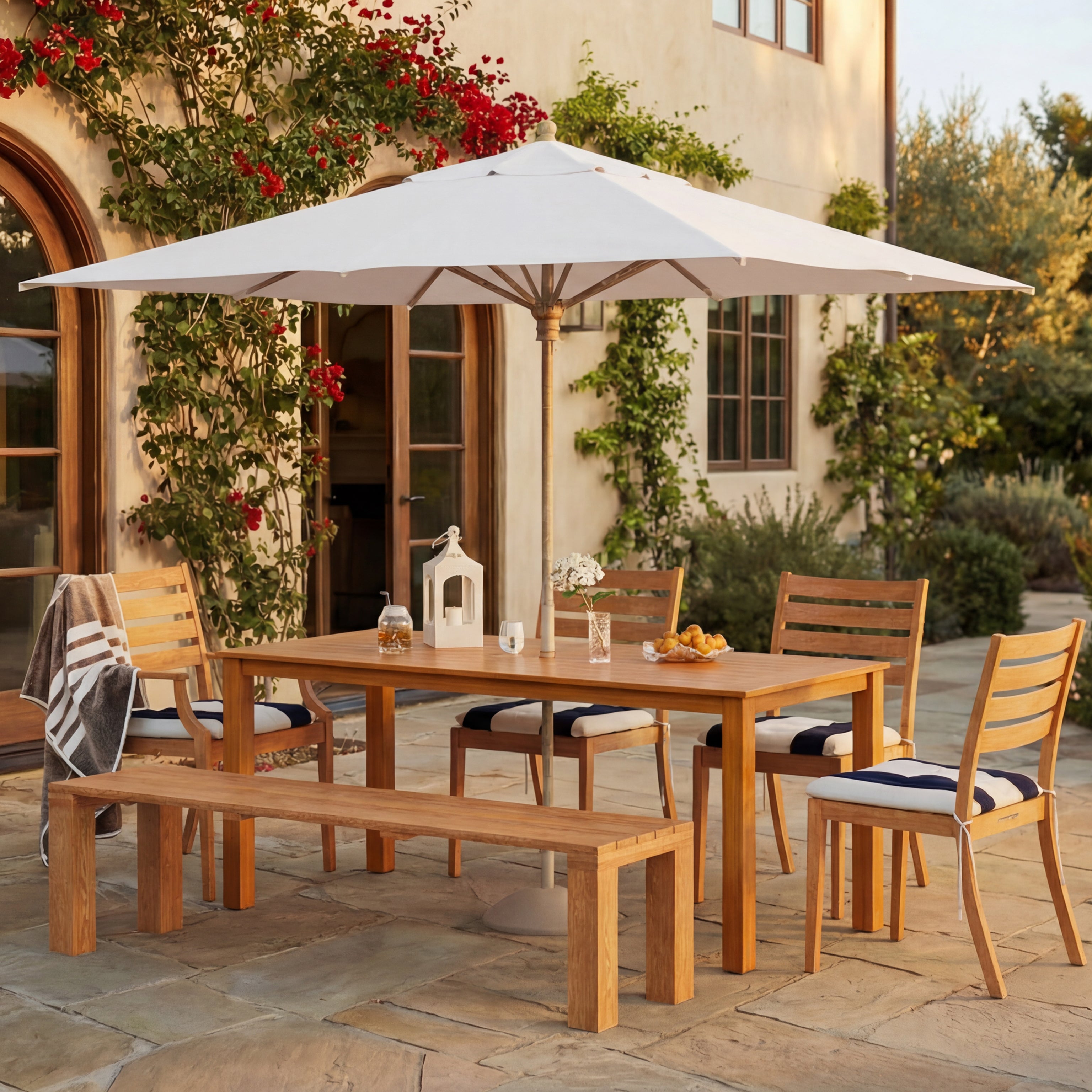 Outdoor dining set with table, chairs, and bench under a large umbrella in a garden setting
